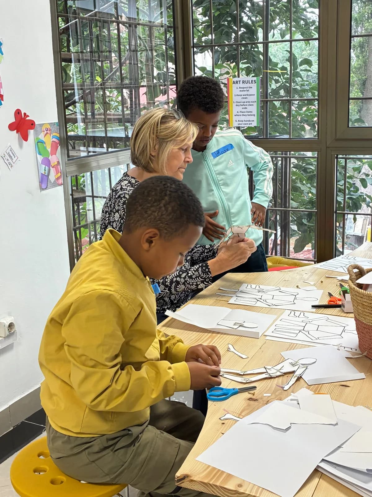 Campers cutting out paper body shapes with their art teacher at the creative studio