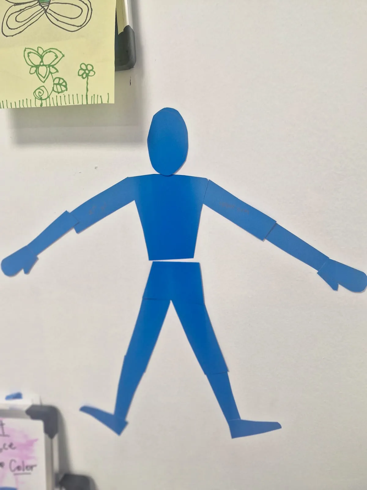 A finished blue paper Shape Man posed mid-stride on the classroom wall