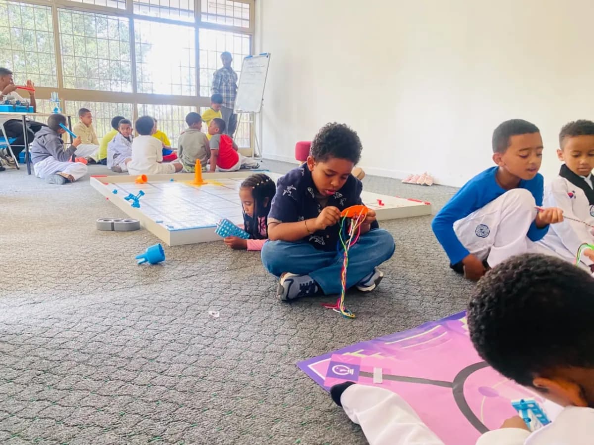 Campers working on floor activity mats, one threading a colorful string toy while others study their coding mats