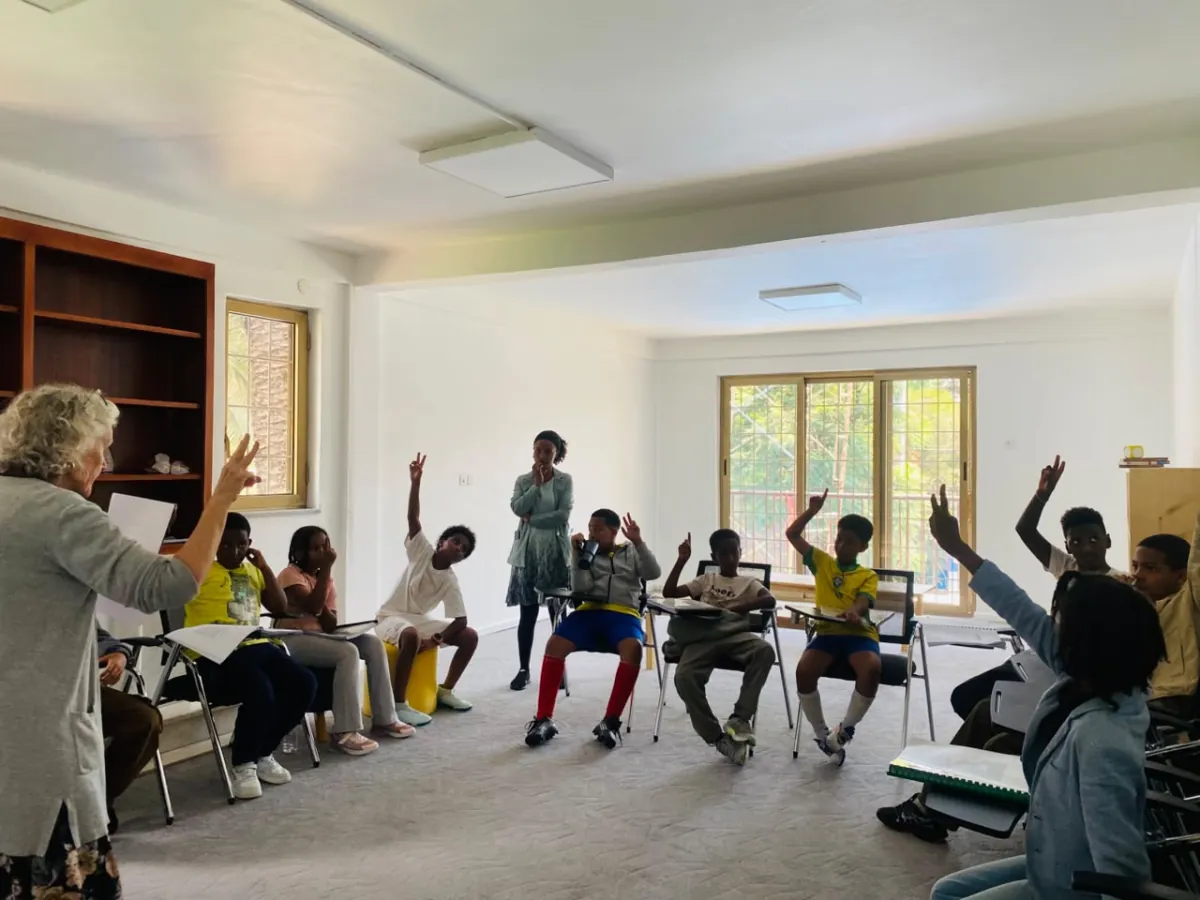 Campers seated in a circle raising their hands to answer while a teacher leads the discussion