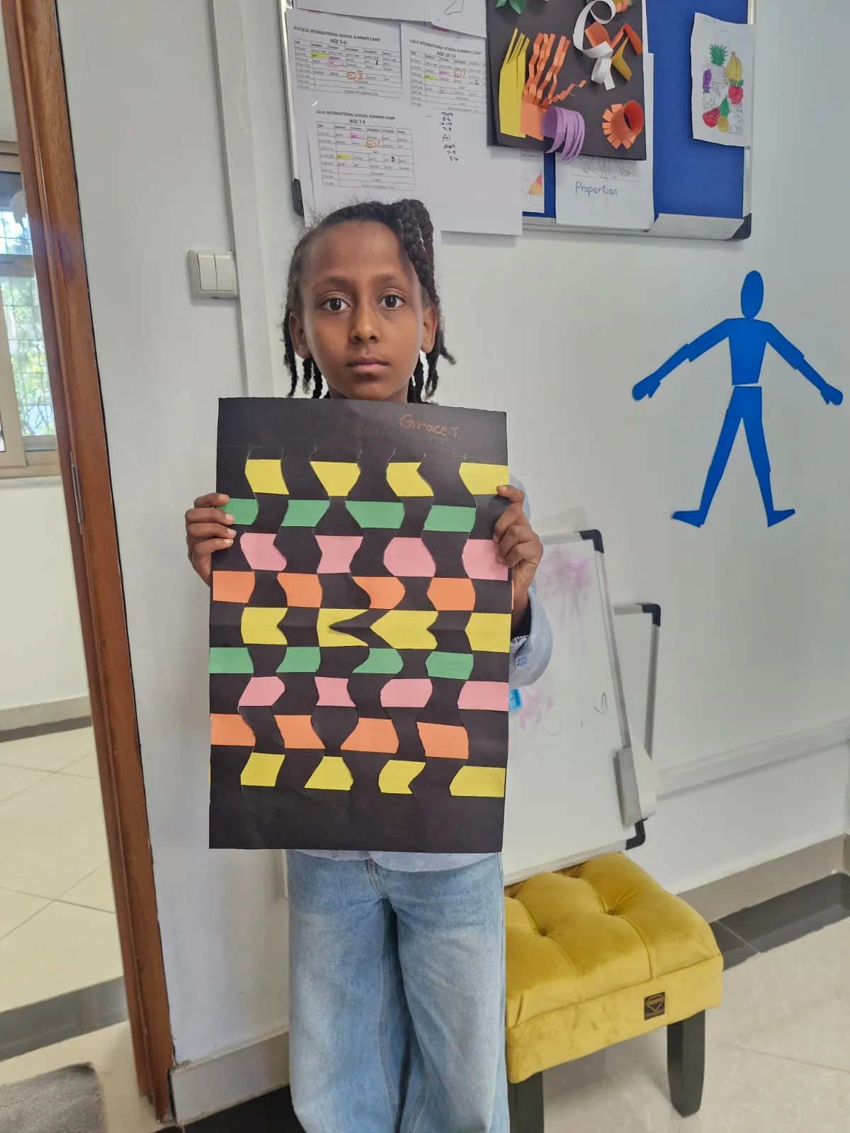 A camper proudly holding up a colorful geometric paper mosaic made of orange, green, yellow and pink shapes