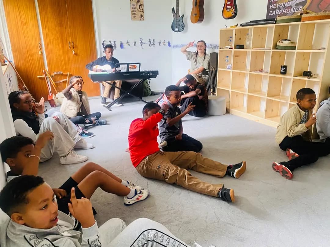 Campers doing movement actions on the music room floor while a teacher plays the keyboard