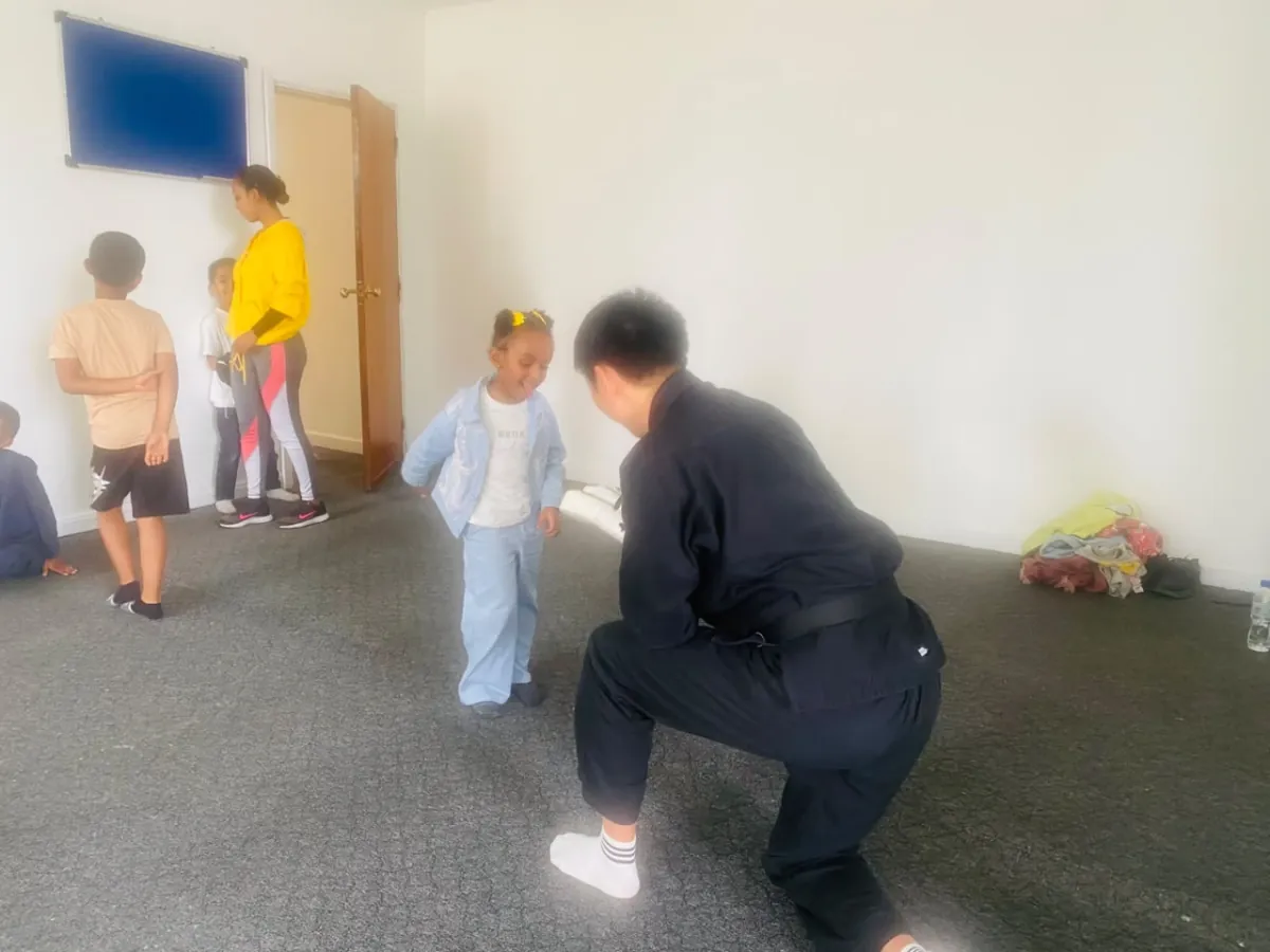 A taekwondo instructor kneeling to coach a young camper through a stance