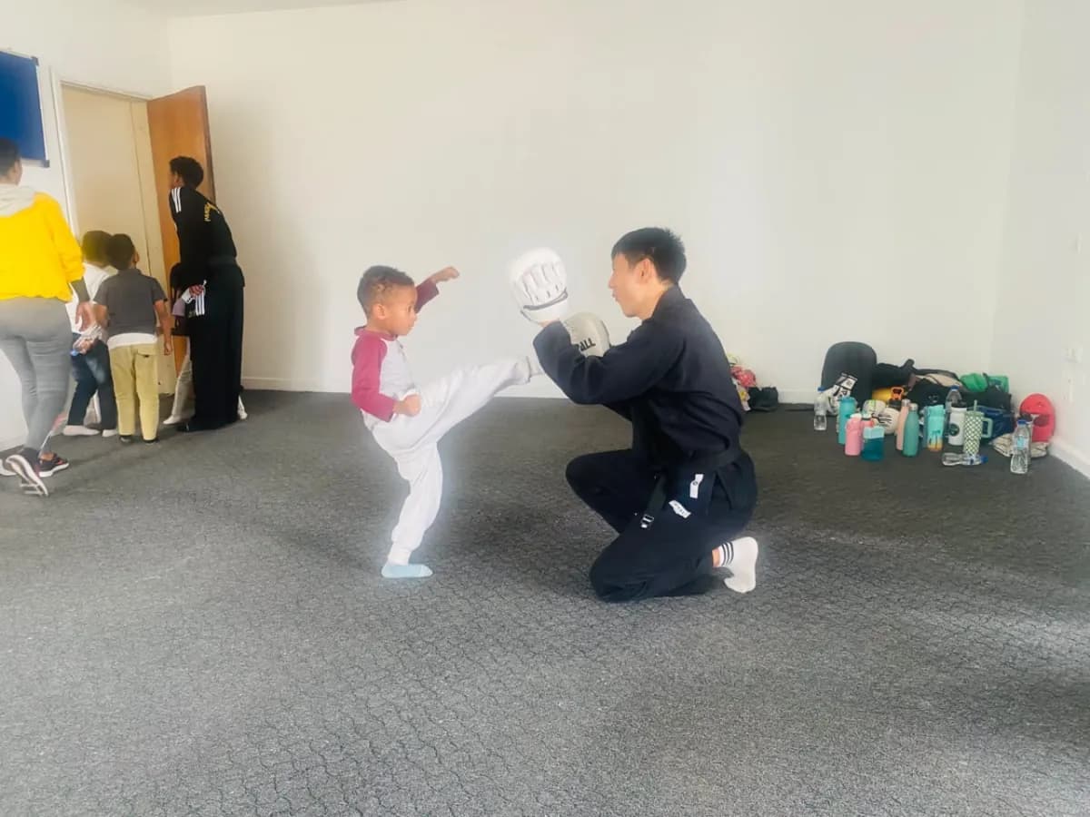 A small camper landing a high kick on a training pad held by the instructor