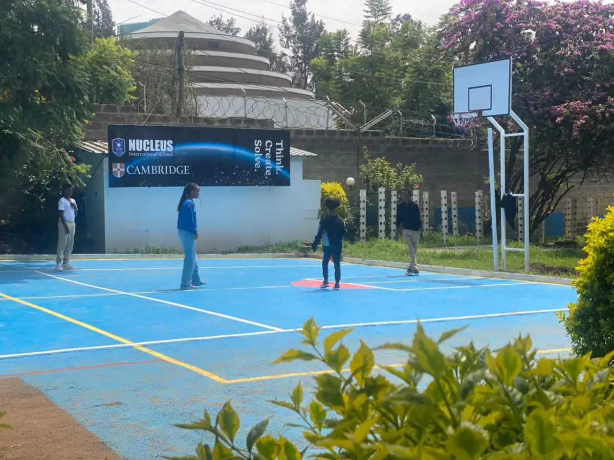 Campers passing a basketball on the blue outdoor court beside the Think Create Solve board
