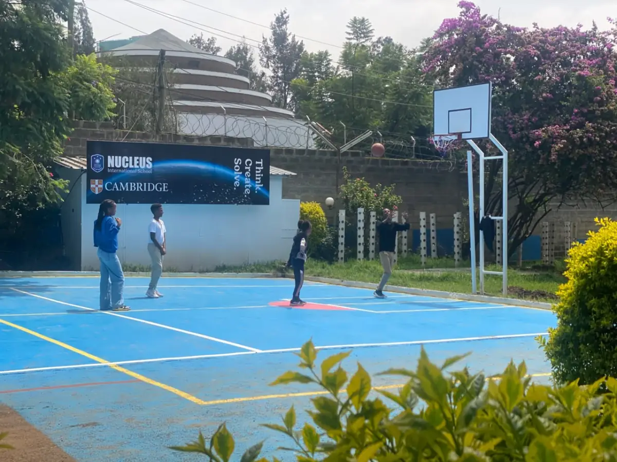 A camper watching her shot arc towards the hoop on the blue outdoor basketball court