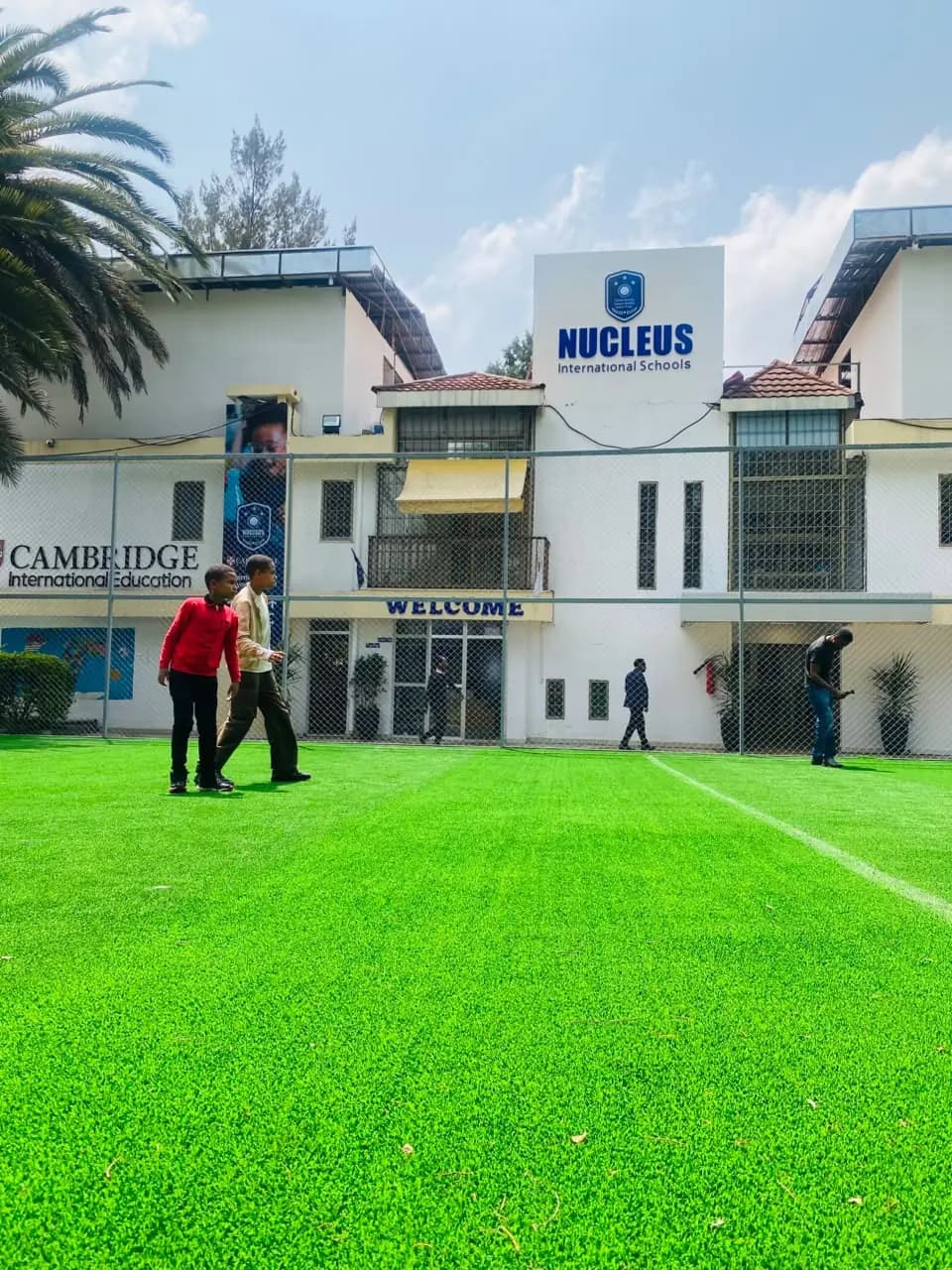 The Nucleus International Schools building and Cambridge banner seen across the green turf pitch