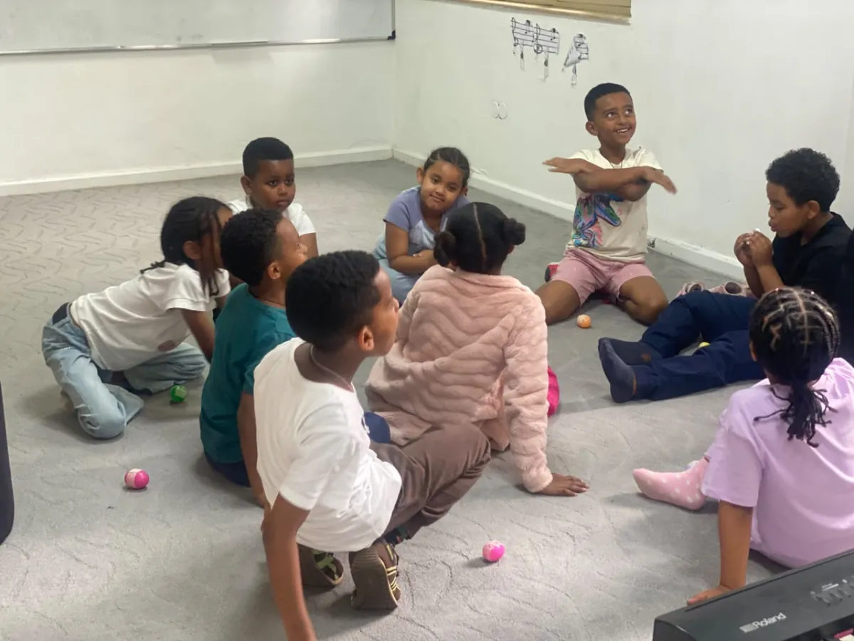 A camper standing with his arms outstretched leading a floor game while the rest of the circle watches him