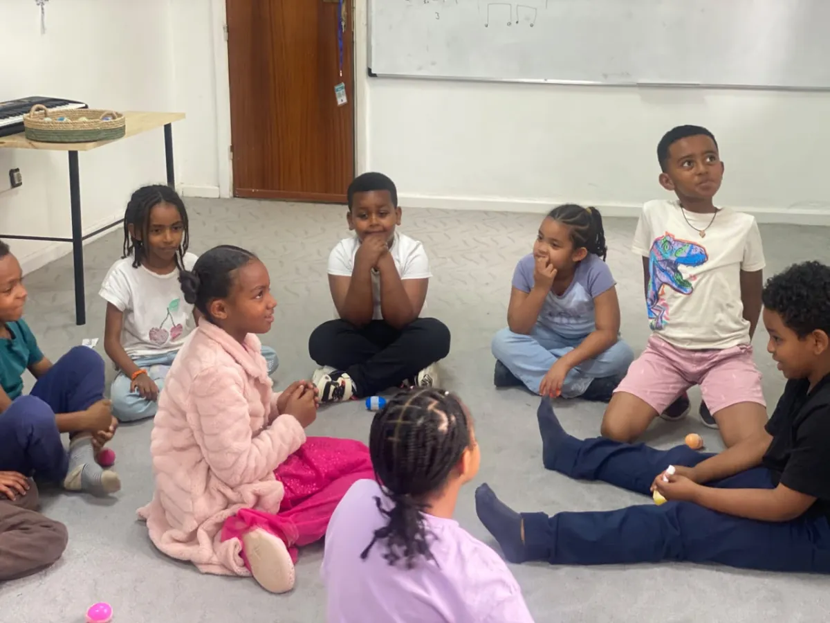 Campers sitting on the floor in a wide circle, laughing and waiting for their turn in the game