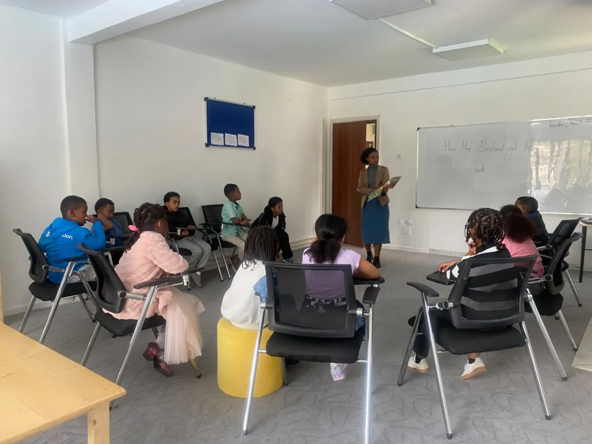 Campers seated in a circle of chairs listening to their teacher during a group session