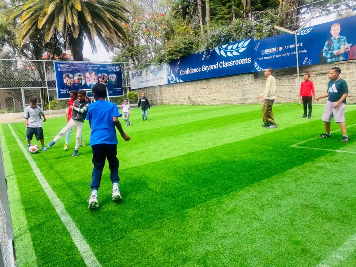 Campers playing football on the turf beneath the Confidence Beyond Classrooms banner