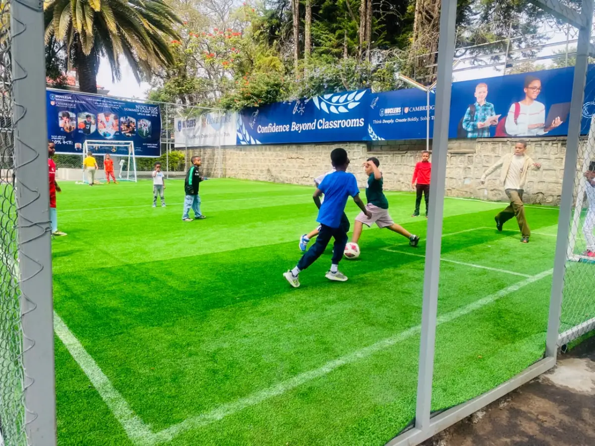Two campers chasing the ball on the turf, seen through the frame of the goal