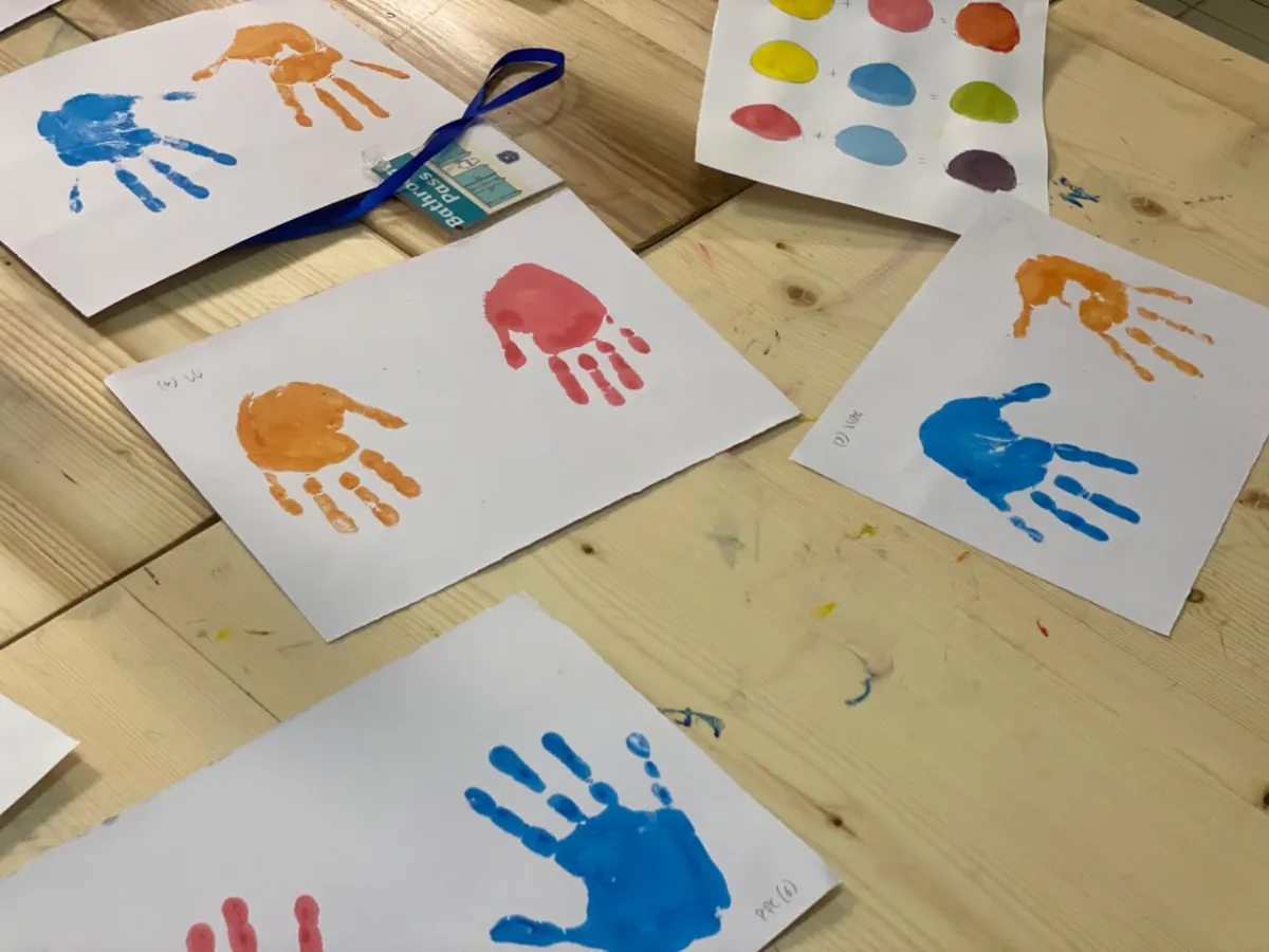 Finished handprint paintings in blue, orange and red drying on the wooden art table
