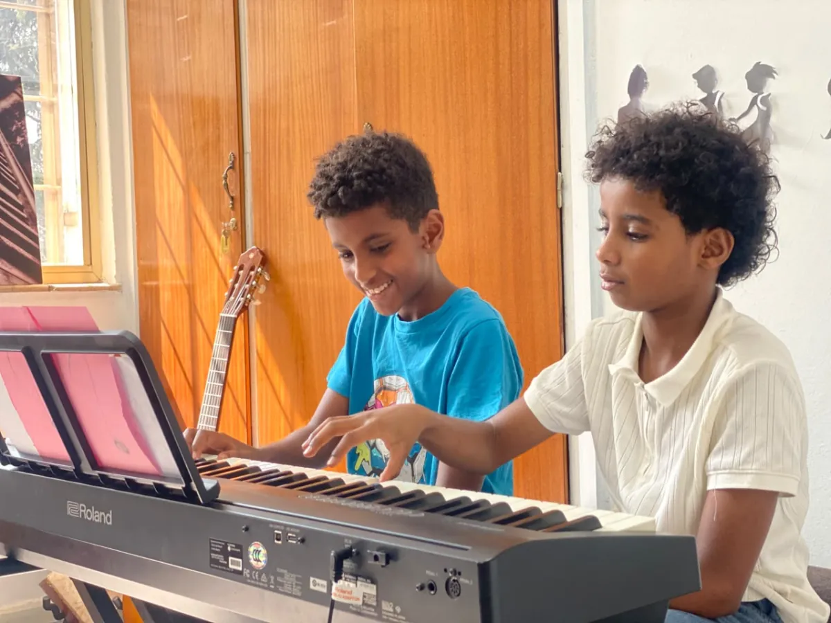 Two campers at the keyboard together, one playing while the other follows the music with a guitar in hand