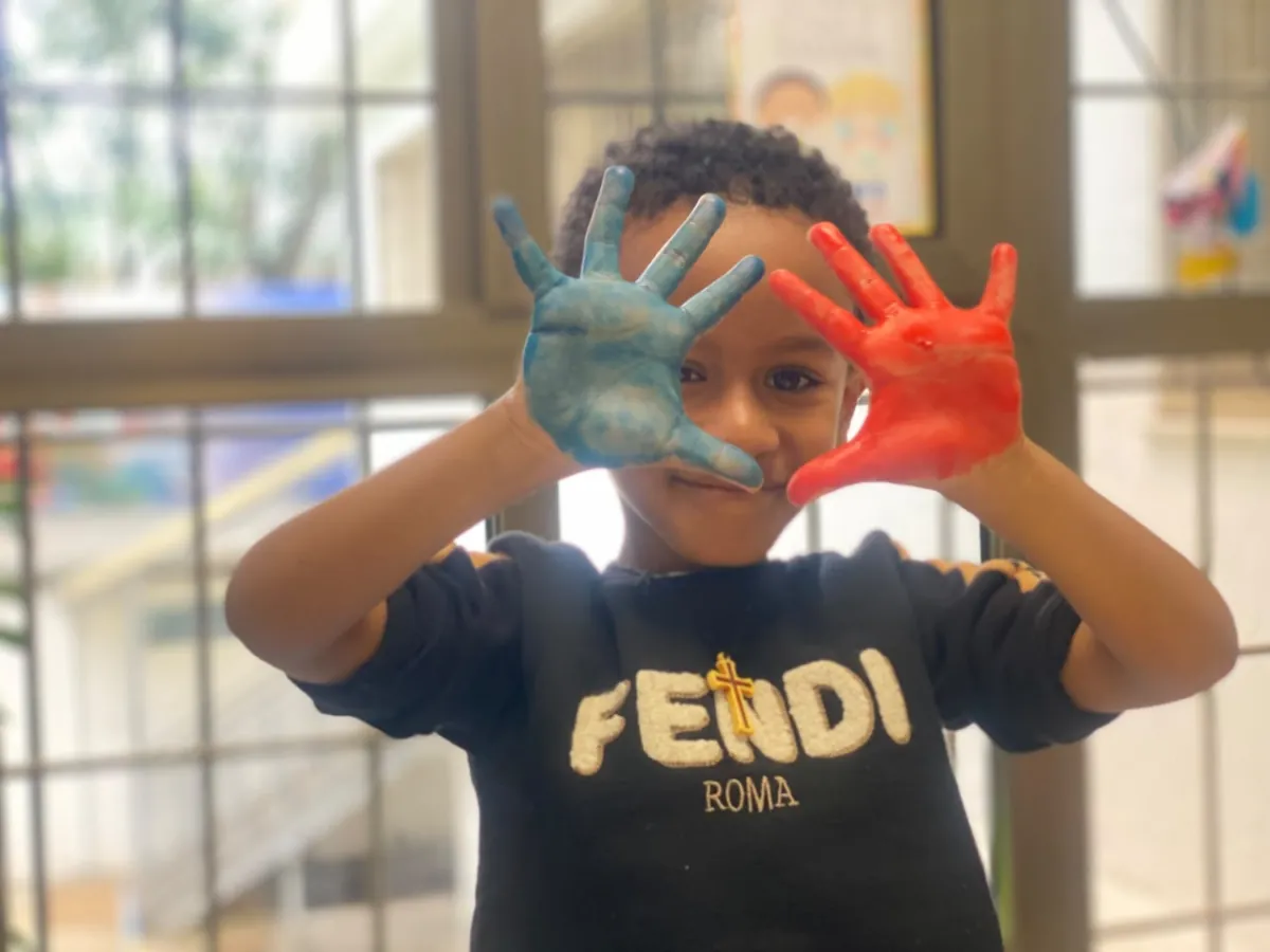 A camper holding up both hands painted blue and red to frame his face