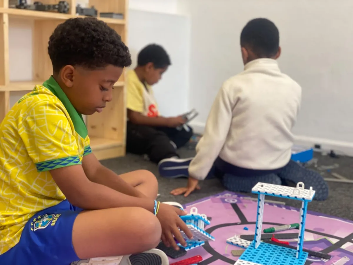 A camper concentrating on his build on the activity mat while a classmate works on a tablet behind him