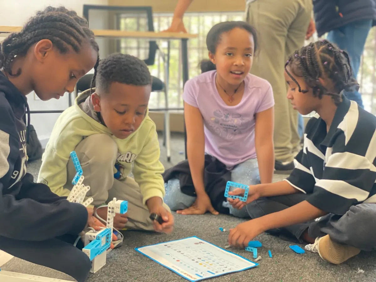 Four campers kneeling around a robot build on the floor, working through the printed instruction card together