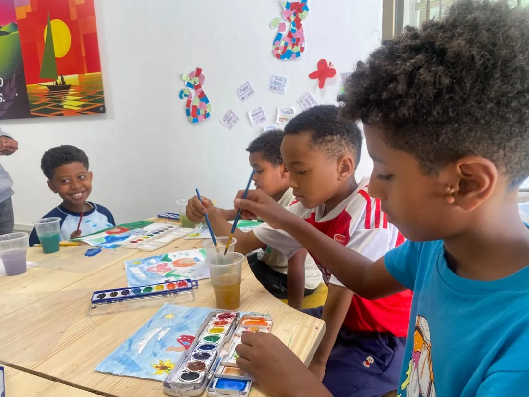 Campers painting watercolour scenes at the art table, paint palettes and water cups in front of them