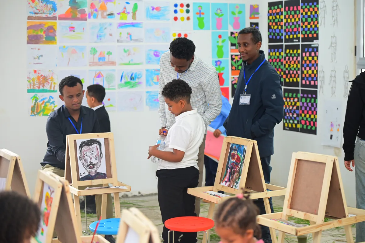 Campers and staff in the art classroom at Nucleus, with childrens paintings covering the wall and portraits standing on easels