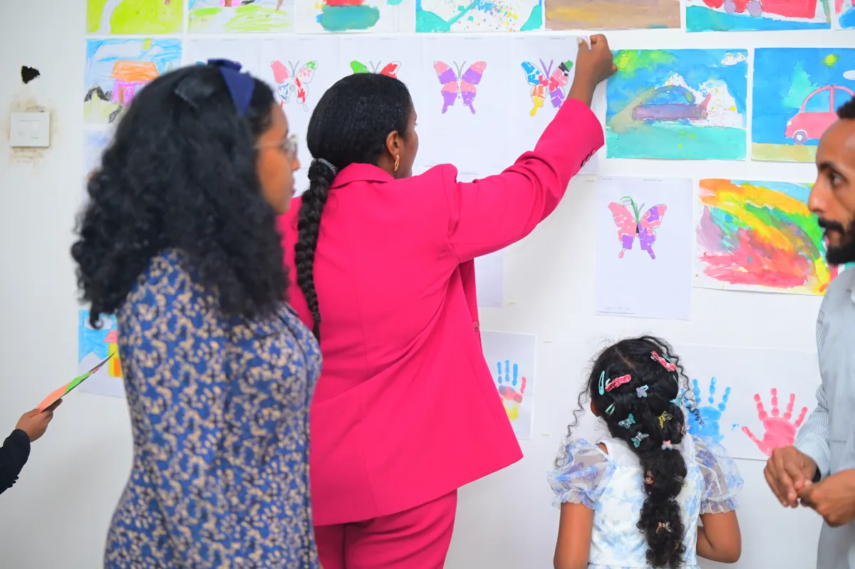 Two members of staff pinning childrens paintings to the display wall in the art room while campers watch
