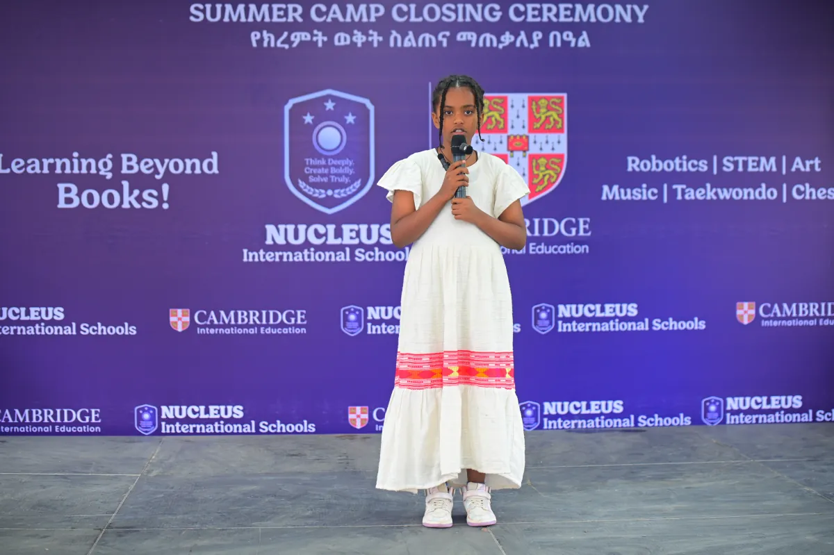 A camper in a traditional white Ethiopian dress presenting at the microphone on stage at the closing ceremony