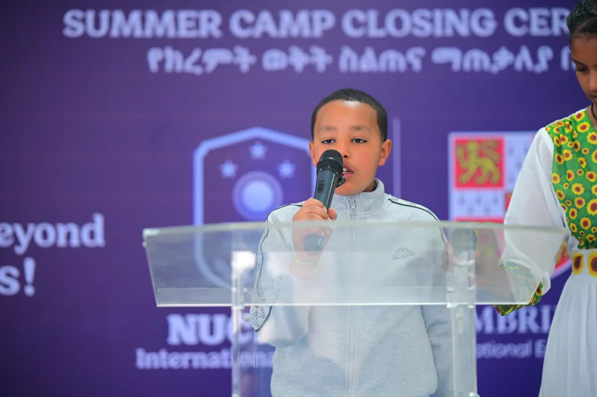 A young camper speaking into a microphone at the podium during the Nucleus summer camp closing ceremony