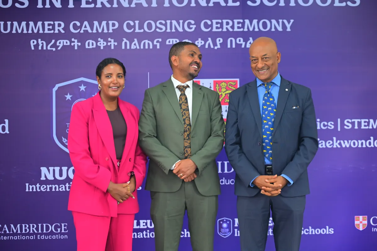 Three members of the Nucleus International Schools leadership team standing together on stage