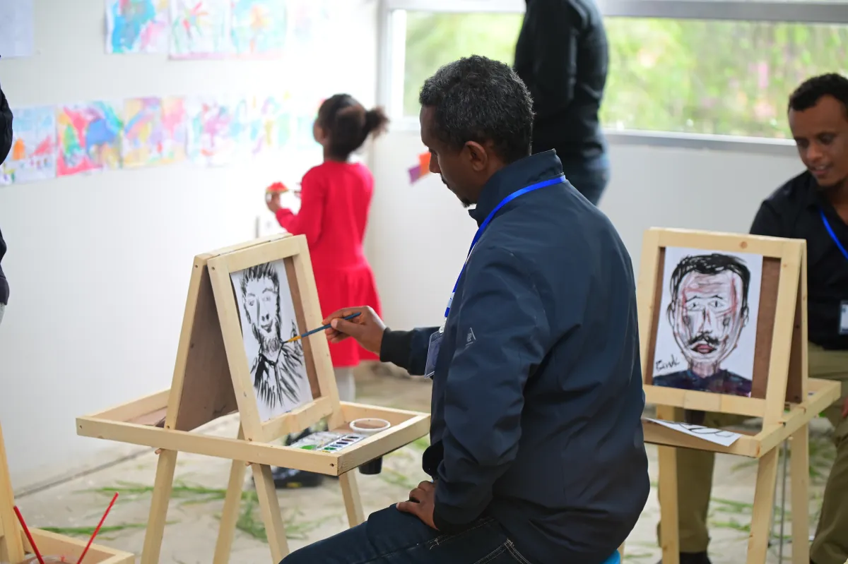 An artist painting a portrait at an easel in the Nucleus art room while campers and parents look on