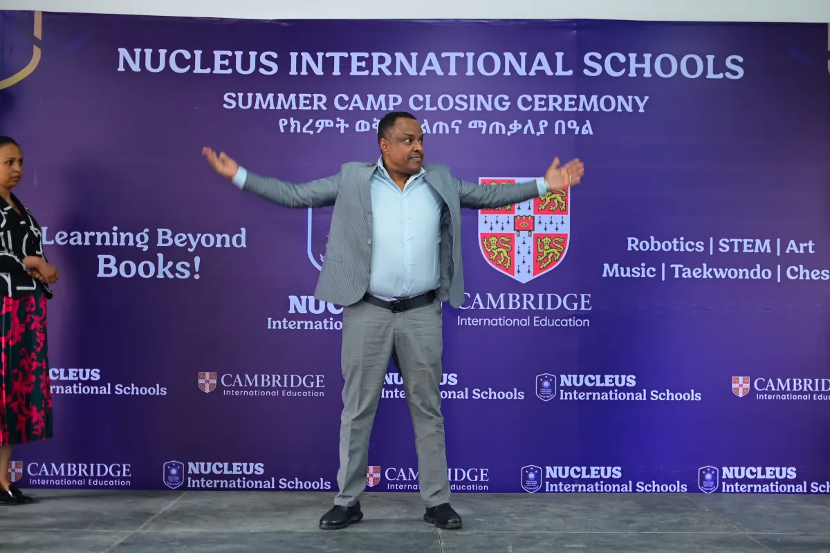 A member of staff on stage with arms open, welcoming campers and families to the closing ceremony
