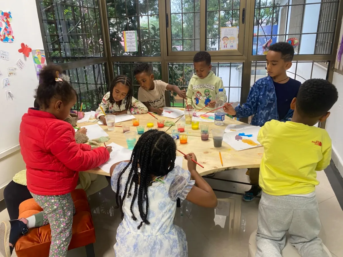 Campers gathered around the art station table mixing paint in plastic cups and working on their own sheets
