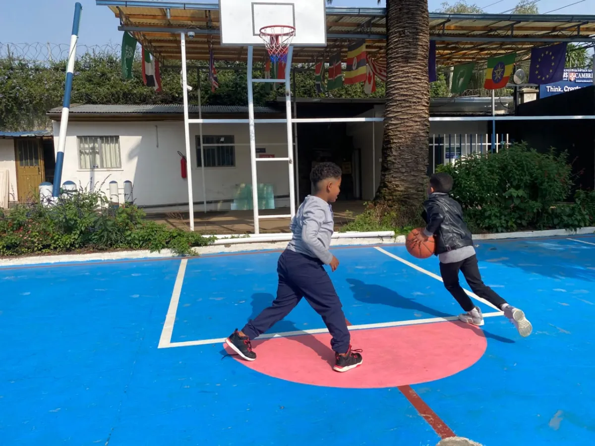 Two campers playing one on one basketball on the blue outdoor court under the palm tree