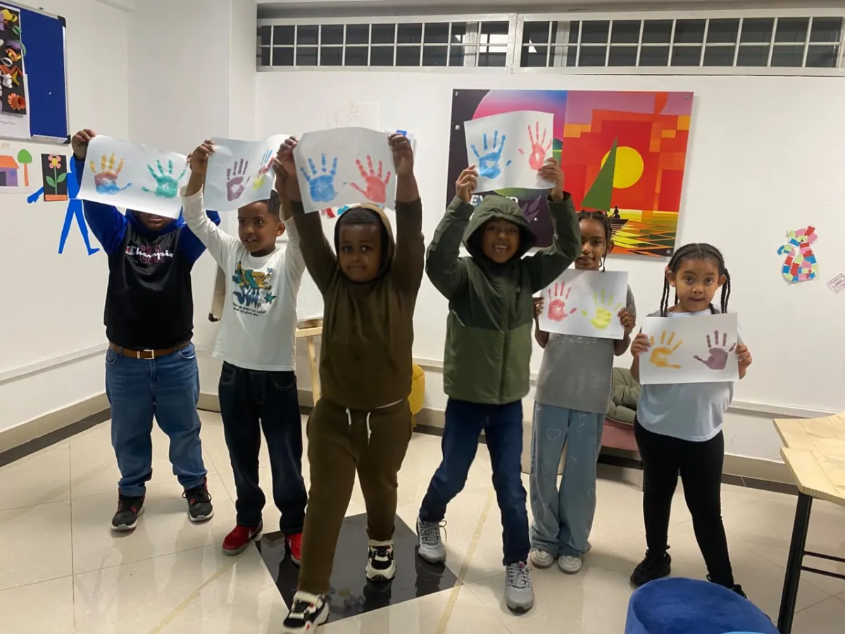 Six campers standing in a line holding their handprint paintings above their heads for the camera