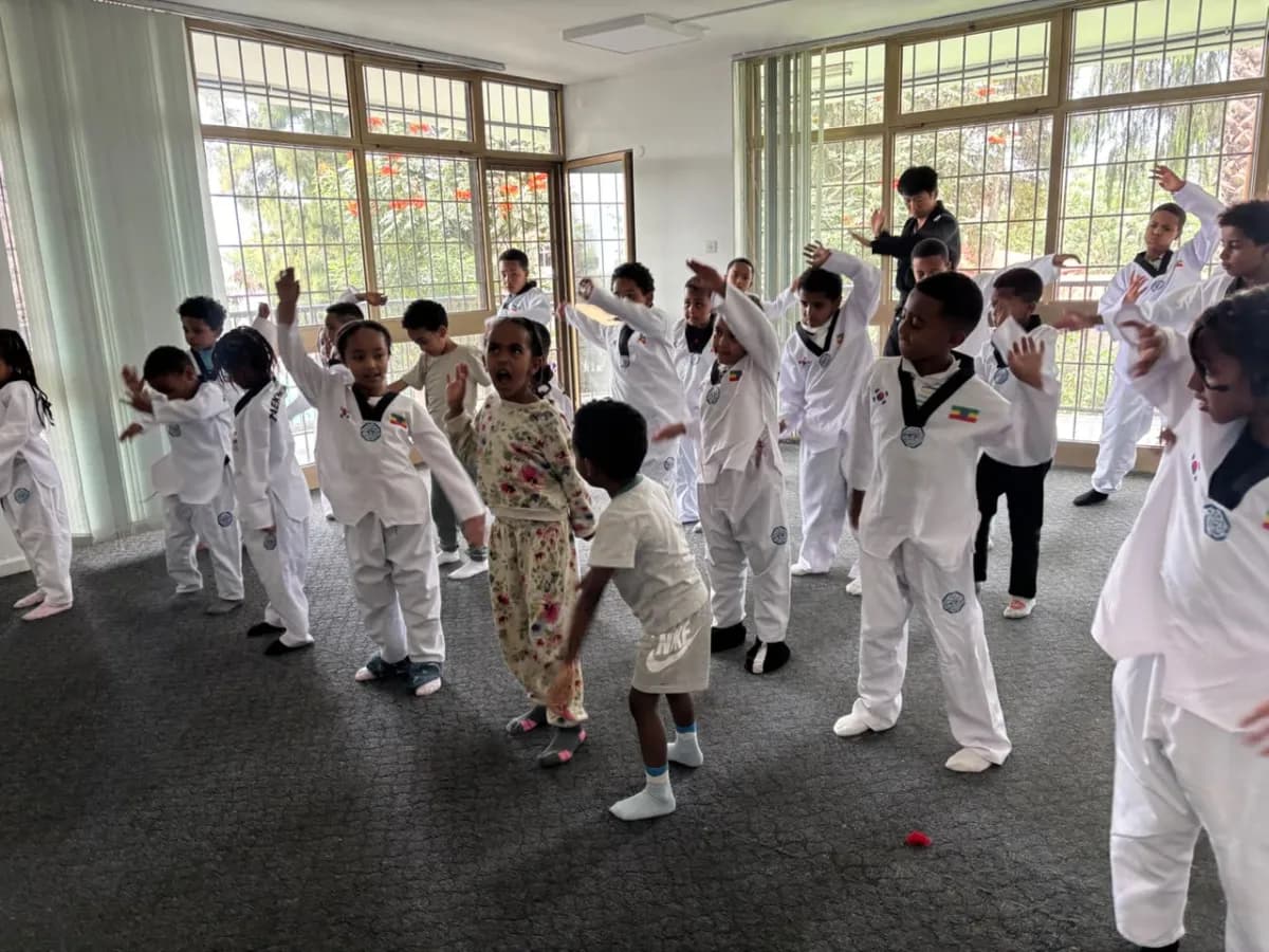 A large group of campers in white taekwondo uniforms practising a blocking pattern in the training hall