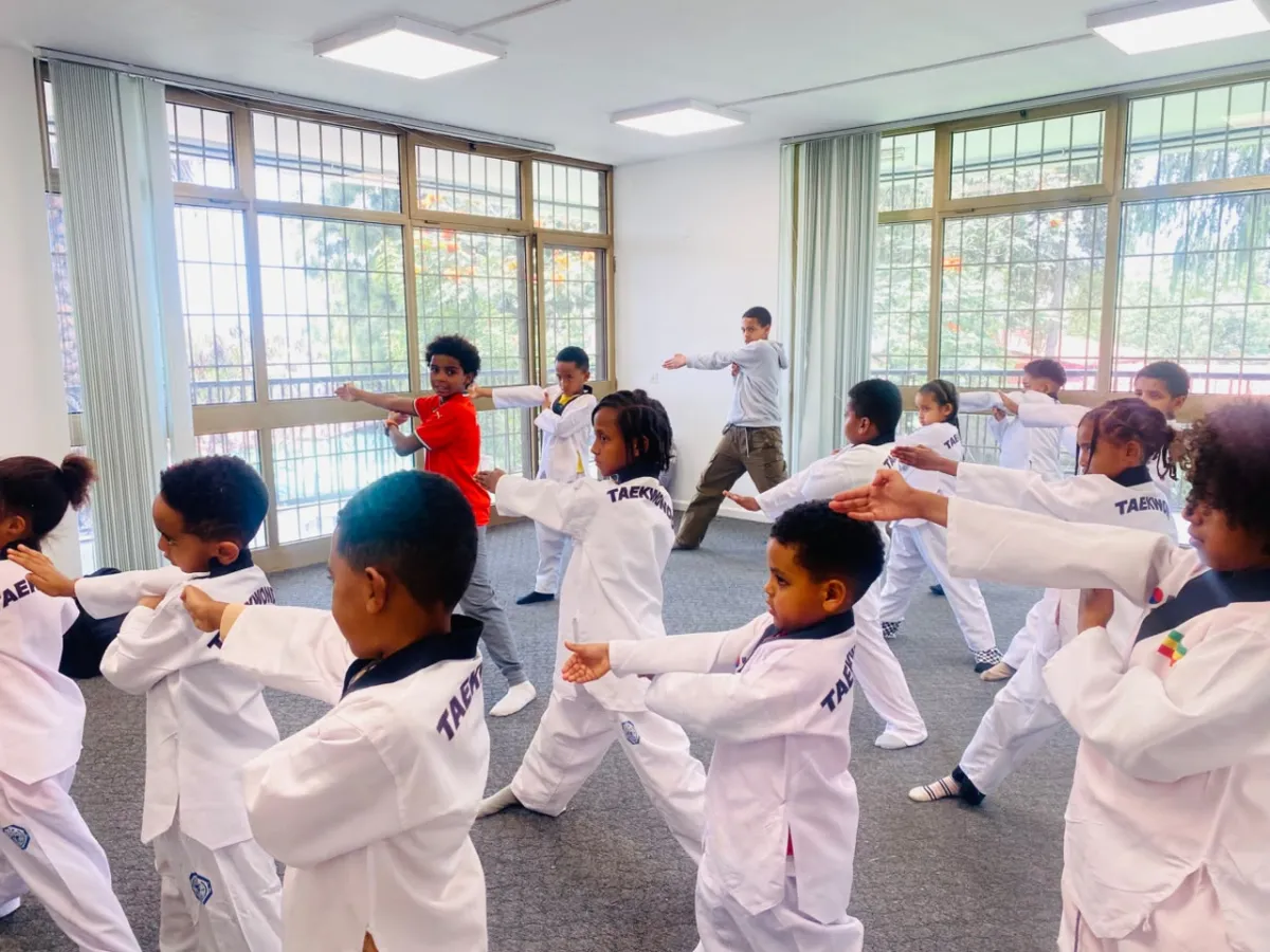 Campers in taekwondo uniforms lined up in rows practising a punch drill with the instructor at the front