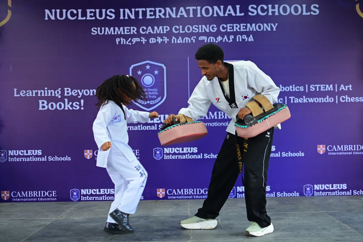 A small child in a taekwondo uniform kicking through a target pad held at her own height by an instructor