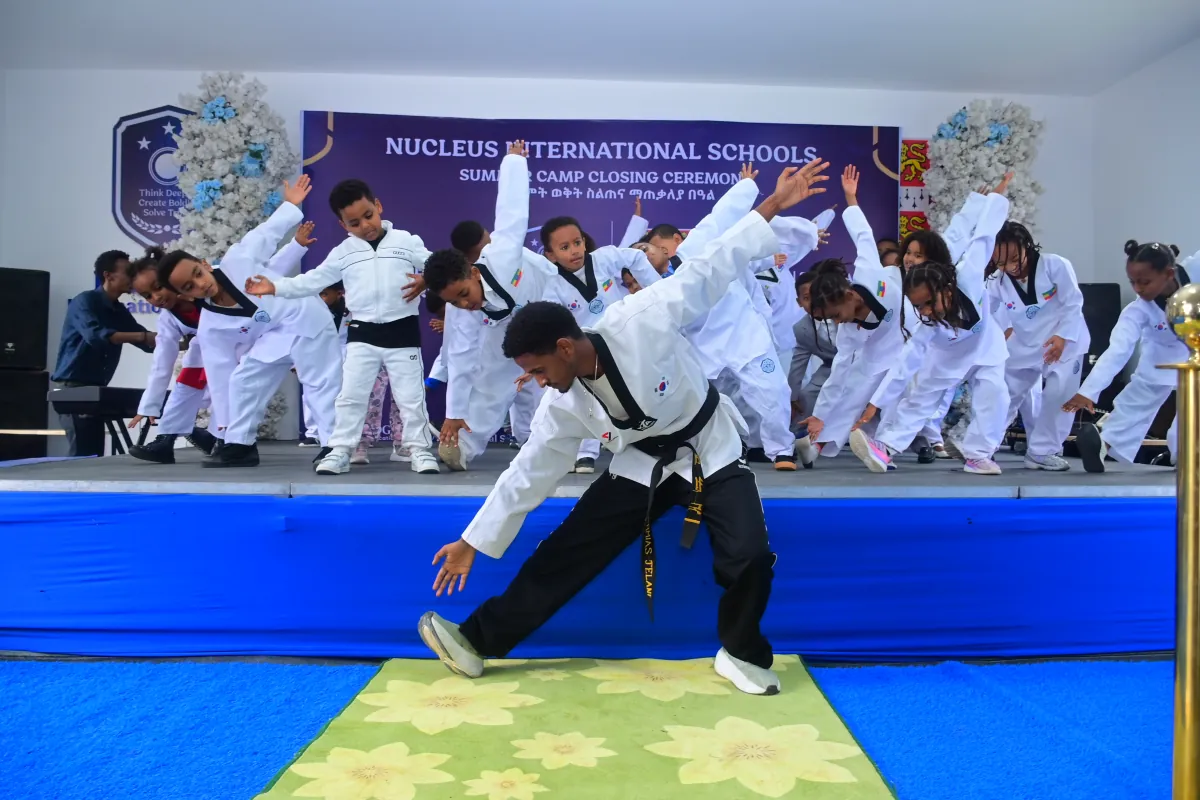 A taekwondo instructor demonstrating a technique while rows of children follow behind him