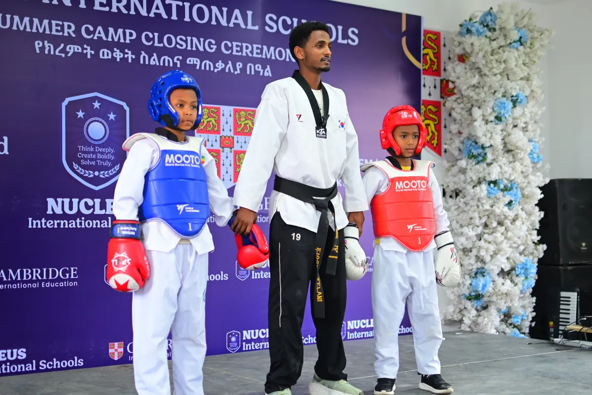 Two young students in red and blue taekwondo sparring gear with their instructor between them
